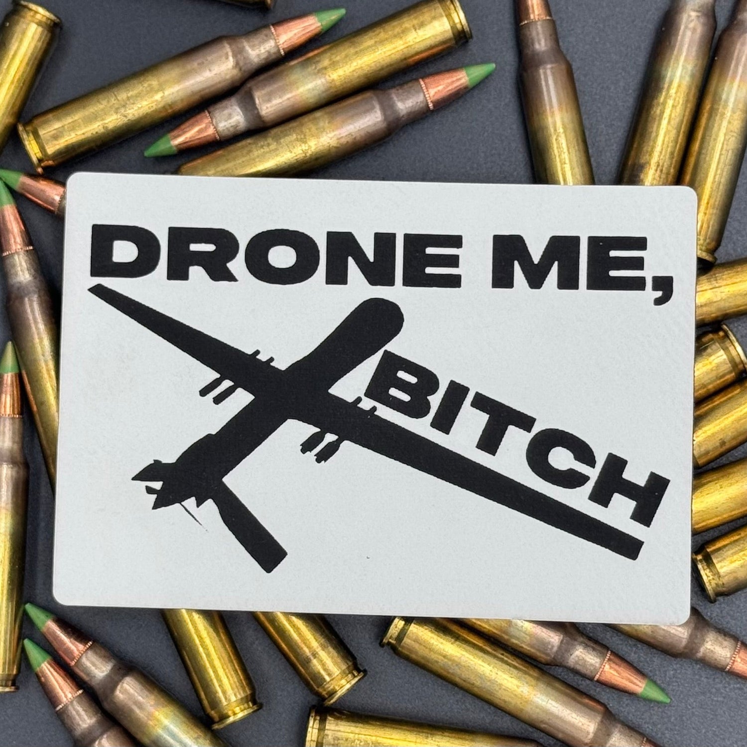 A white leatherette patch of a reaper drone and the text 'Drone Me, Bitch' on a bed of ammo