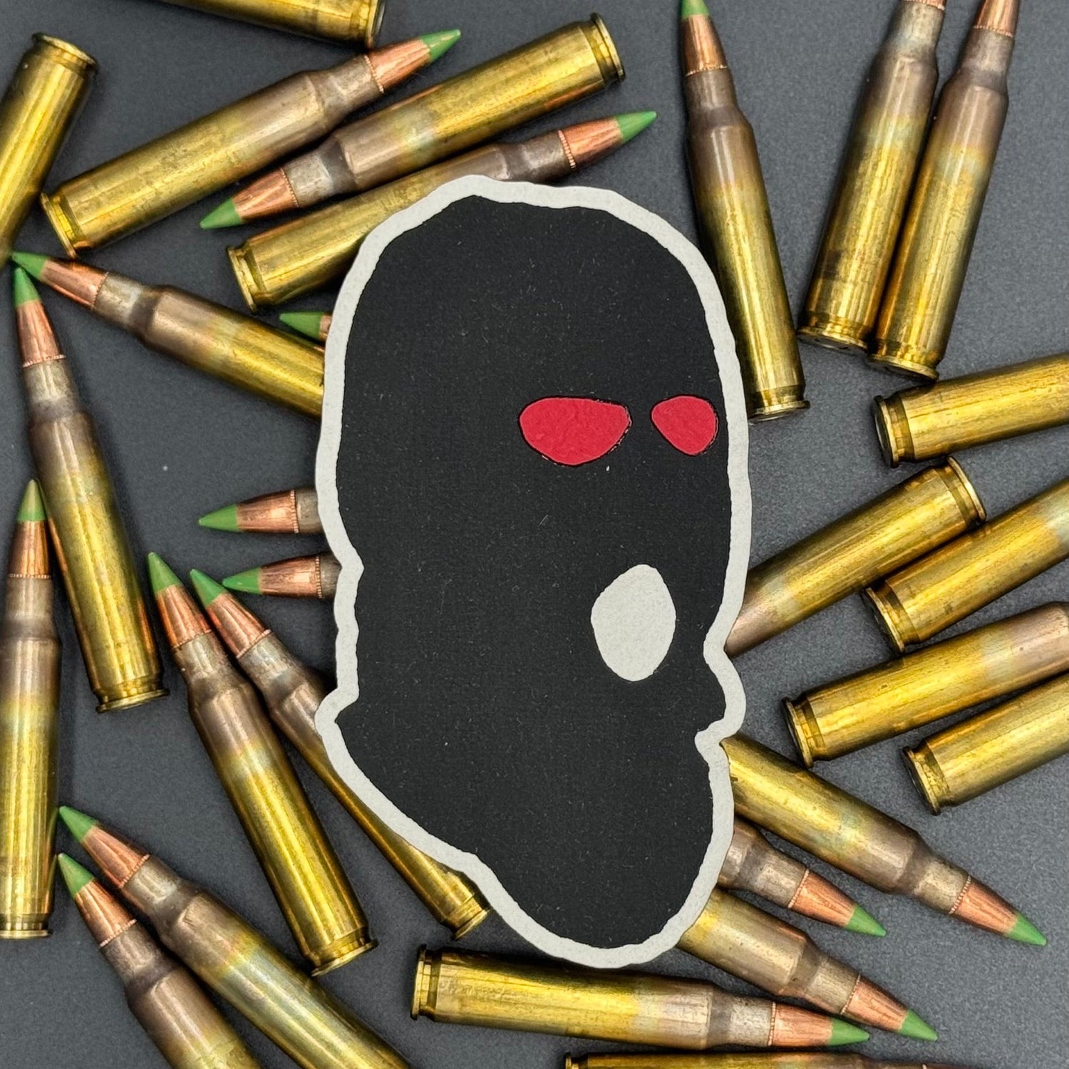 A leatherette patch of a worn ski mask with red eyes on a bed of ammo