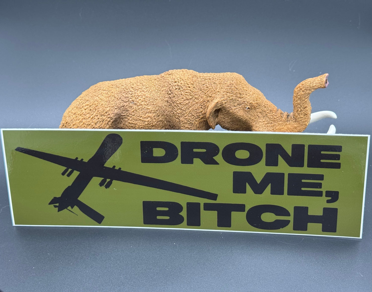 A bumper sticker in OD green with a reaper drone and the text