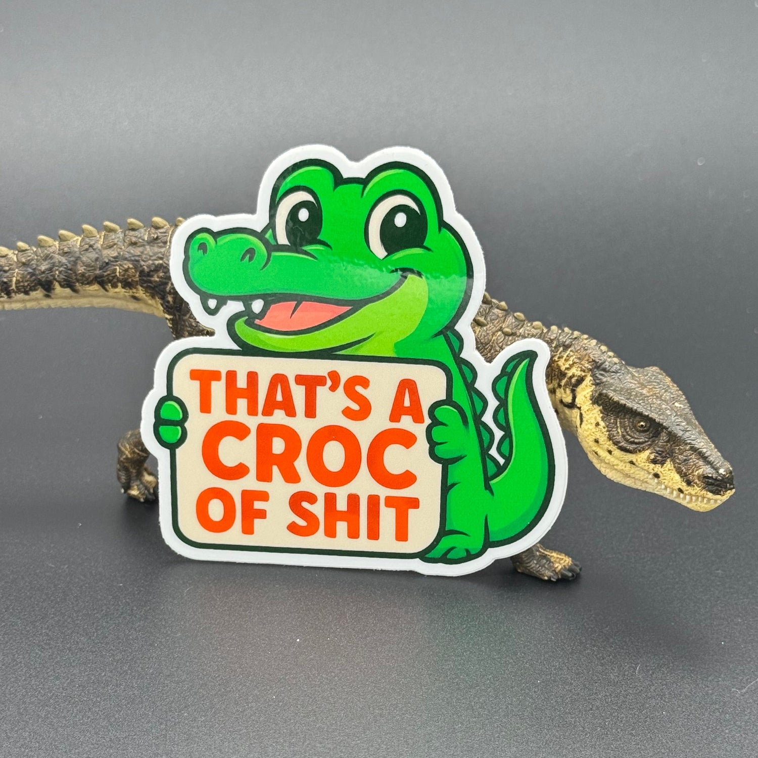 Sticker of a Green Cartoon Crocodile holding a sign saying