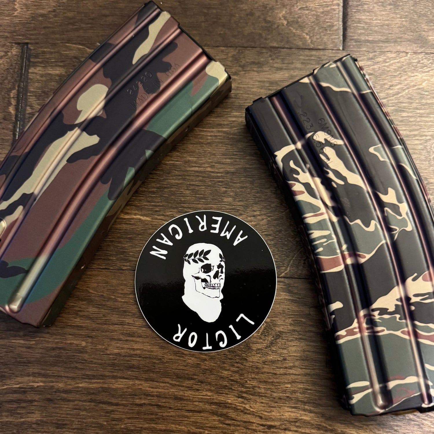 Two camouflage magazines on a wooden surface with a 'American Victor' badge in the center.