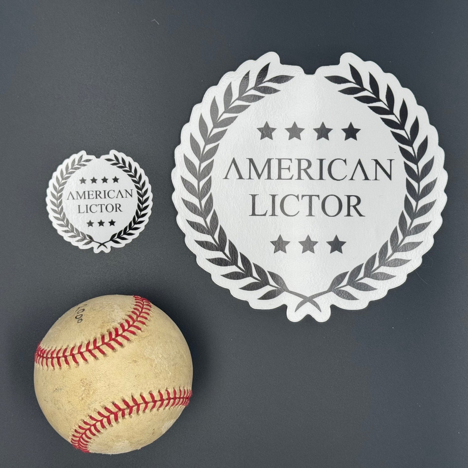 Sticker of an XL American Lictor Logo in white pictured with a baseball for scale