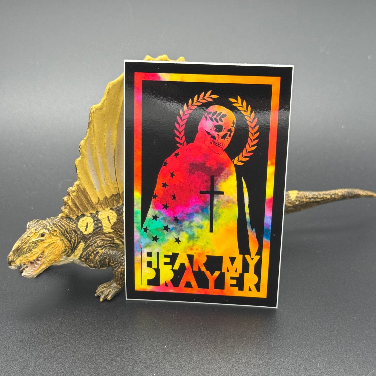 Chromatic sticker of a man draped in the American Flag with the text 'Hear my Prayer' posing with a dinosaur