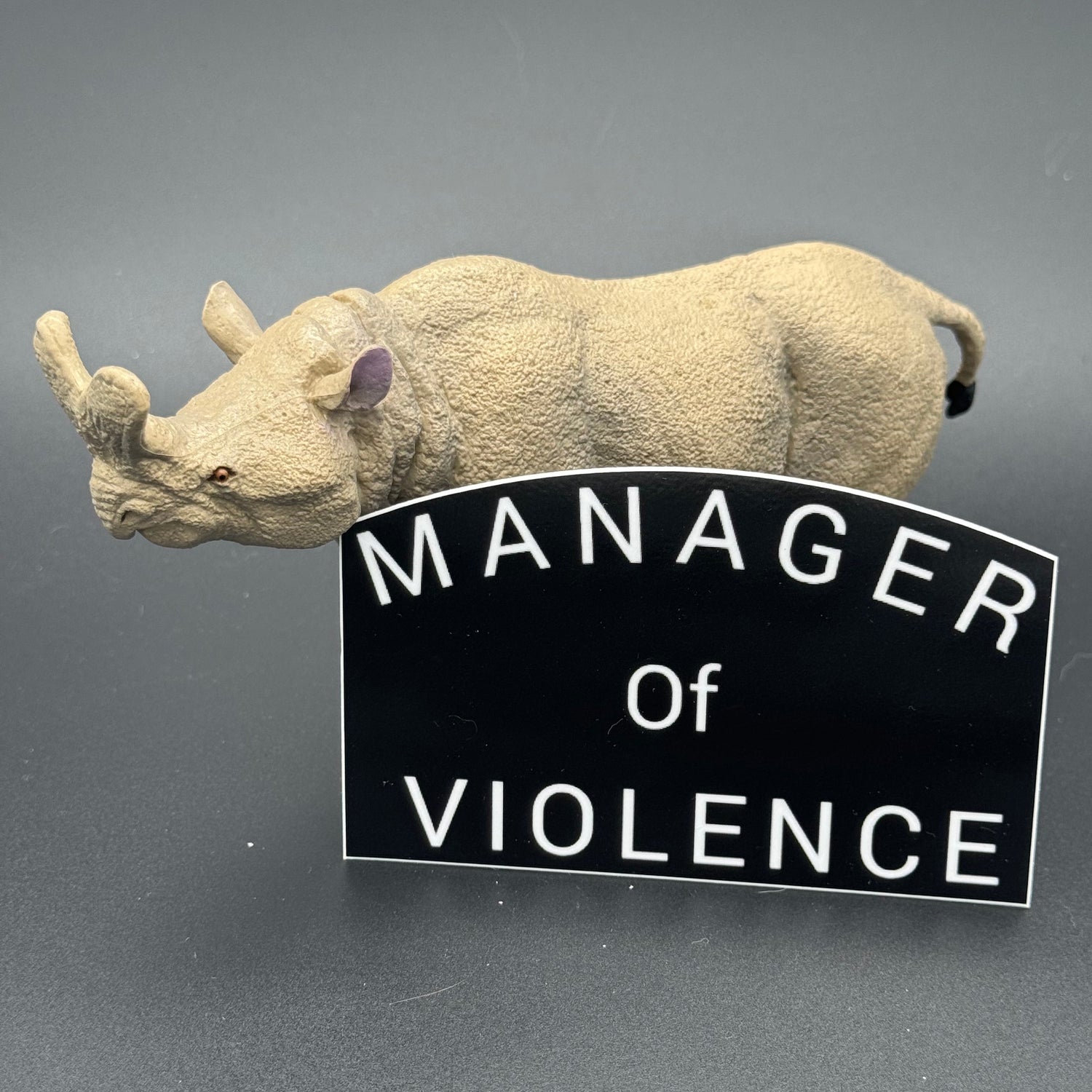 Black sticker with the text 'Manager of Violence' posing with a prehistoric mammal