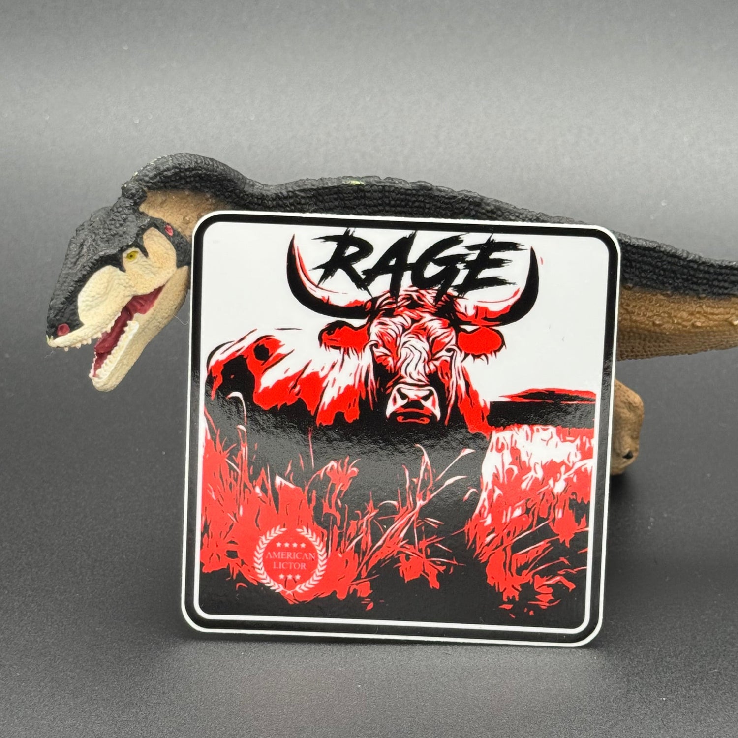 Black, red and white sticker of a bull with the text 'Rage' posed with a dinosaur