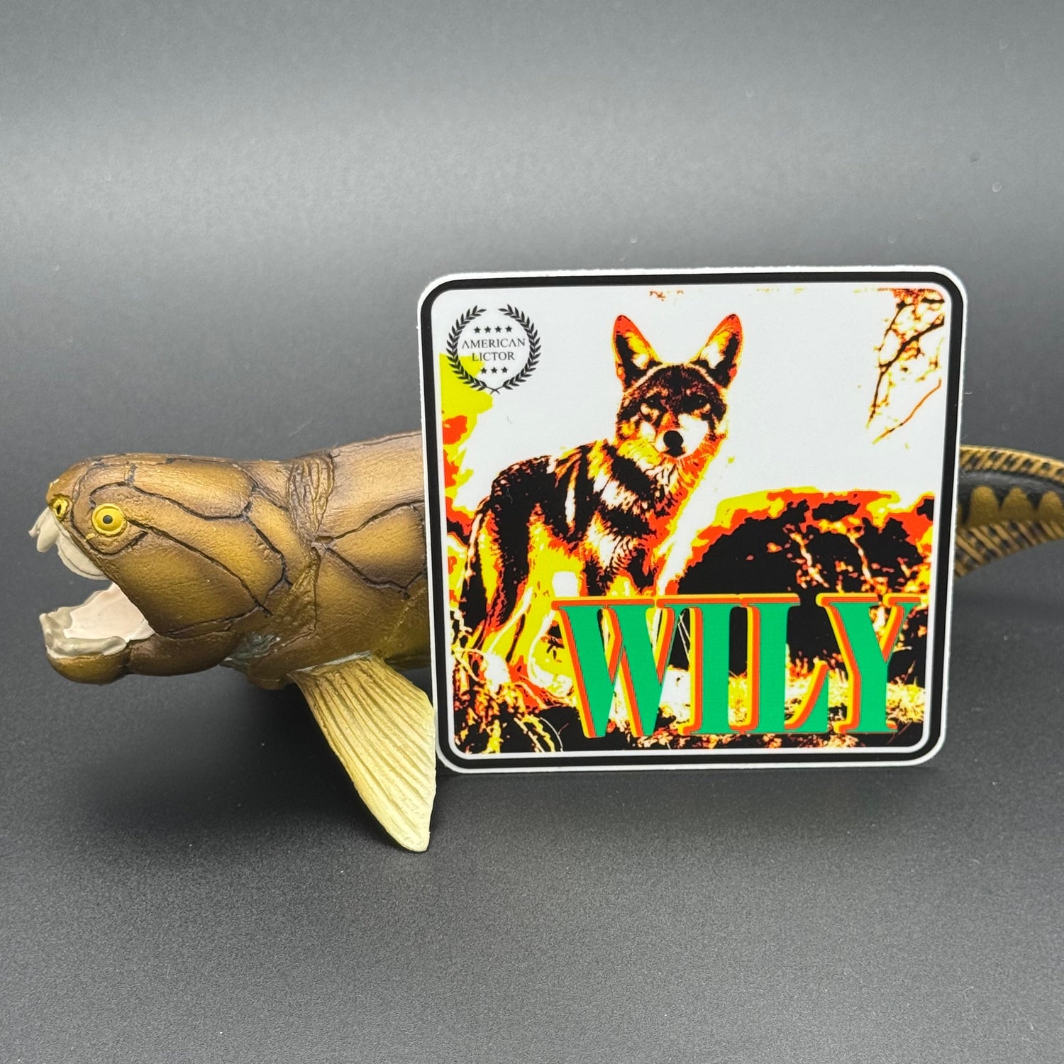 Multicolor sticker of a coyote with the text 'Wily' posed with a Dunklesteus