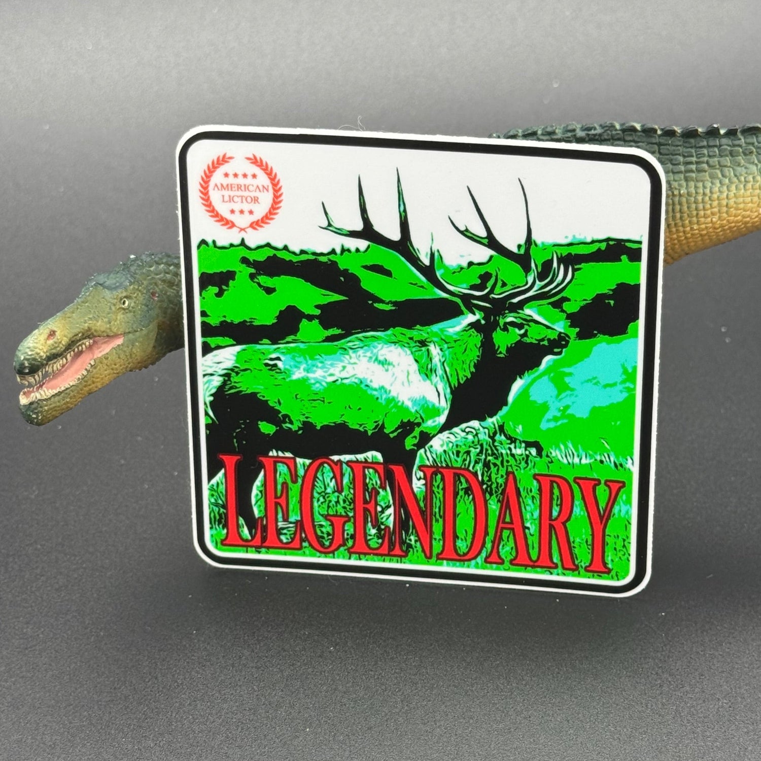 Green, red an White sticker of an elk with the text 'Legendary' posed with a dinosaur