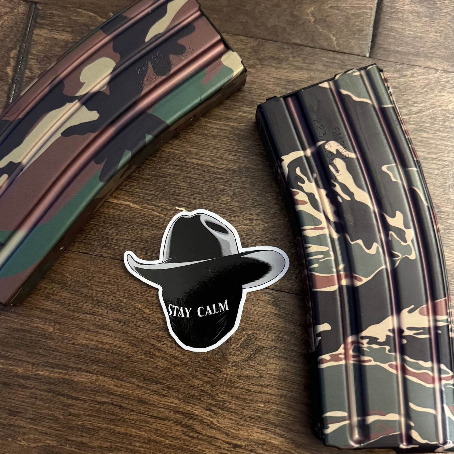 Camouflage magazines on a wooden surface with a 'Stay Calm' sticker and cowboy hat