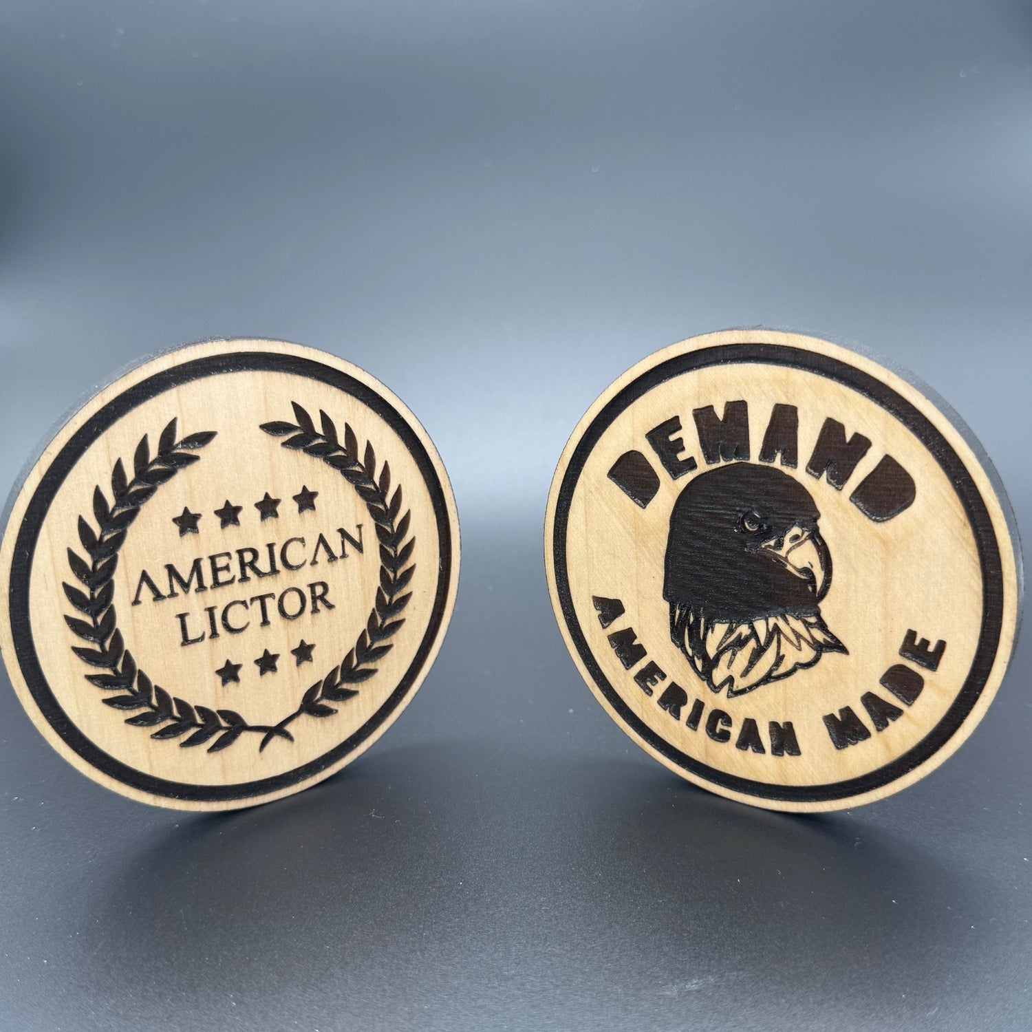 Two circular wooden coasters with the American Lictor Laurel Logo and 'Demand American Made' Designs