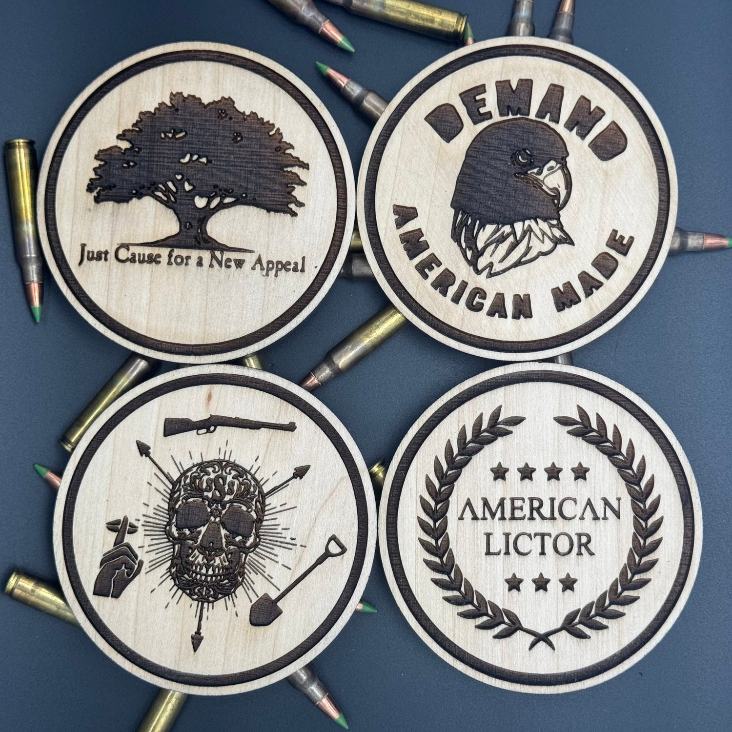 Four circular wooden coasters with engraved designs of American Lictors best selling designs on a bed of ammo