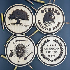 Four circular wooden coasters with engraved designs of American Lictors best selling designs on a bed of ammo