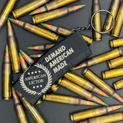 A black keychain shaped like an AR15 mag with the American Lictor logo and slogan Demand American Made' on a bed of ammo