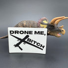 A white leatherette patch of a reaper drone and the text 'Drone Me, Bitch' posed with a dinosaur