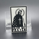 A white leatherette patch with a man with a skeleton mask draped in the American Flag with a Laurel Halo and cross and the text 'Hear my Prayer'