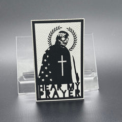 A white leatherette patch with a man with a skeleton mask draped in the American Flag with a Laurel Halo and cross and the text 'Hear my Prayer'