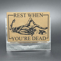 A leatherette patch in beige picturing a skeleton wearing colonial soldier clothing with a tomahawk and the text 'Rest when you're dead"