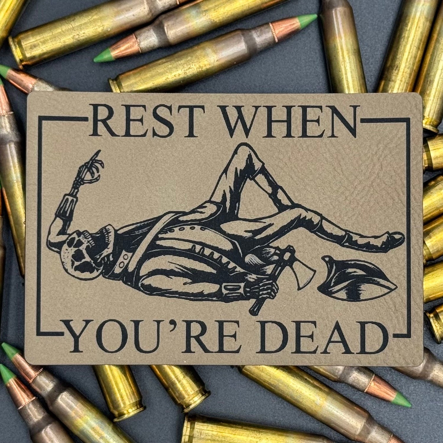 A leatherette patch in beige picturing a skeleton wearing colonial soldier clothing with a tomahawk and the text 'Rest when you're dead
