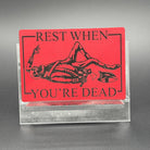 A leatherette patch in red picturing a skeleton wearing colonial soldier clothing with a tomahawk and the text 'Rest when you're dead"