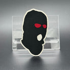 A leatherette patch of a worn ski mask with red eyes