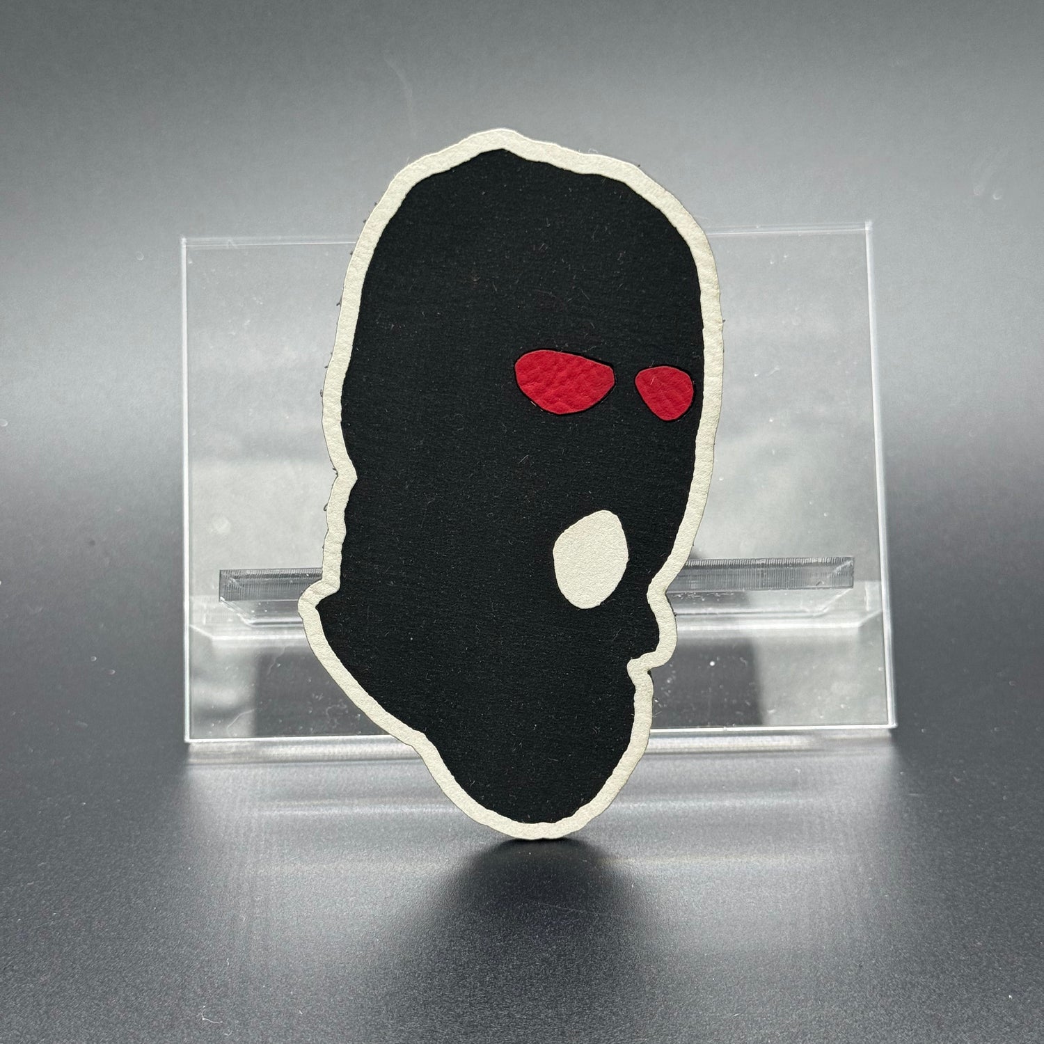 A leatherette patch of a worn ski mask with red eyes