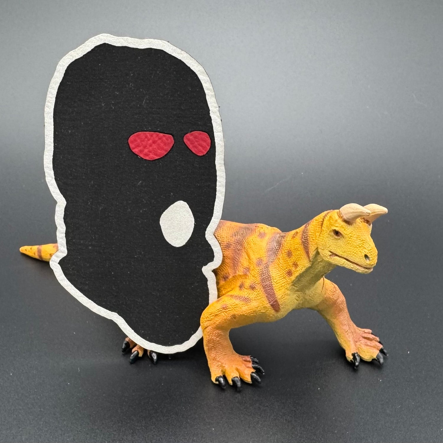 A leatherette patch of a worn ski mask with red eyes posed with a dinosaur