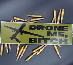A bumper sticker in OD green with a reaper drone and the text "Drone Me, Bitch" on a bed of ammo