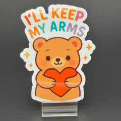 Sticker of a Brown Cartoon bear holding a heart saying "I'll keep my arms"