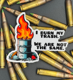 Sticker of an oil drum fire with the American Lictor Logo and the text "I burn my trash we are not the same" on a bed of ammo