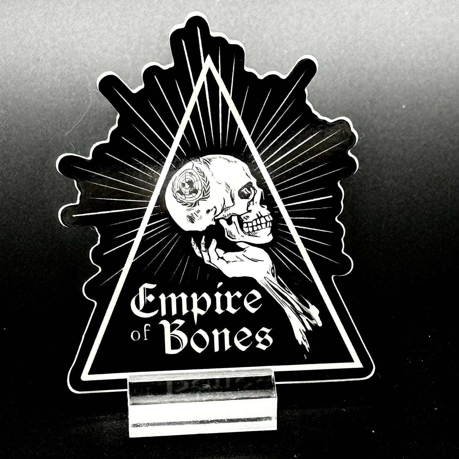 Sticker of a triangle with a hand holding a skull with the UN logo with the text 'Empire of Bones'