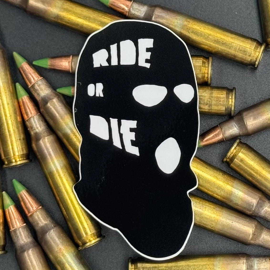 Sticker of a black ski mask with the text 'Ride or Die' on a bed of ammo