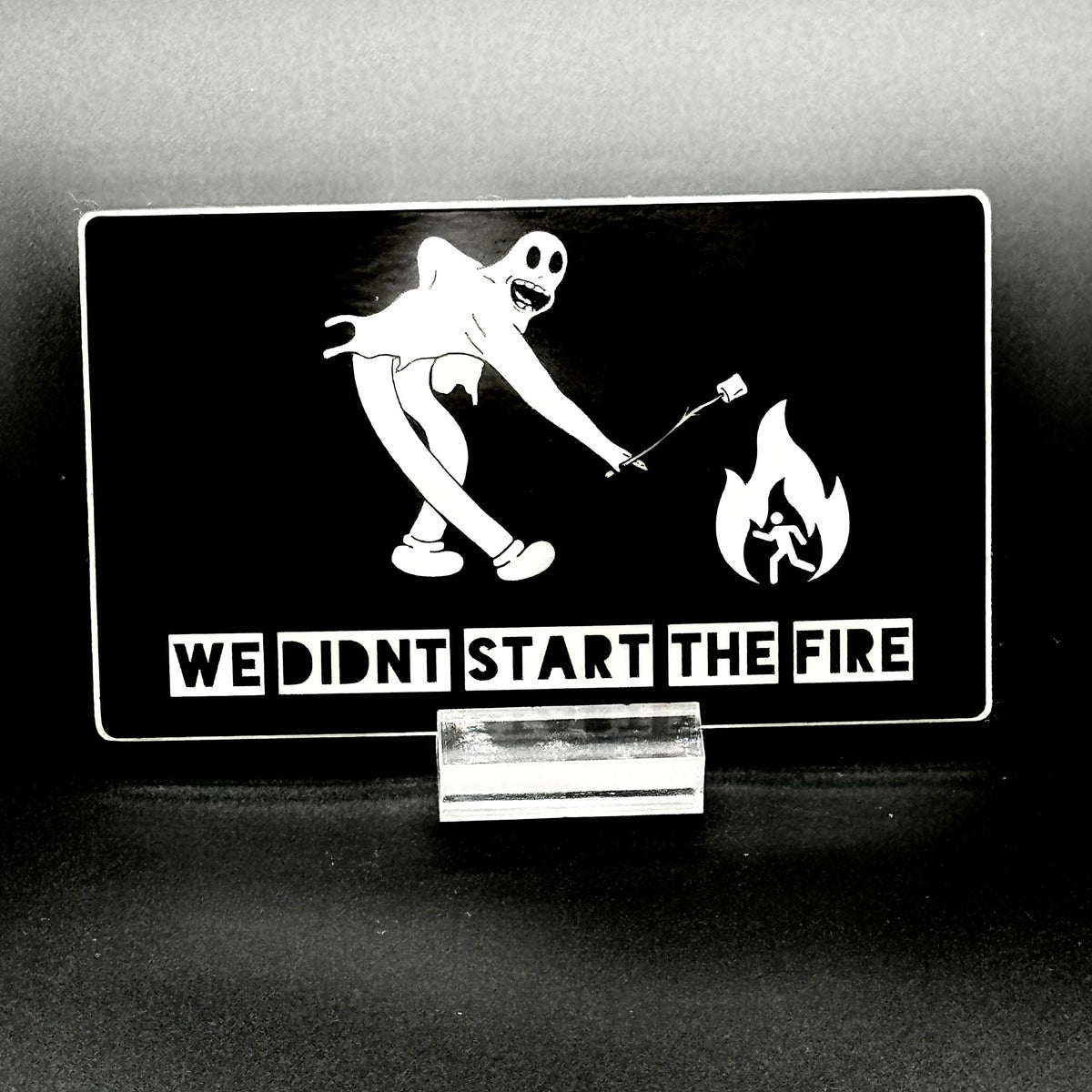 Sticker of a cartoon character in a ghost suit roasting a marshmallow over a fire