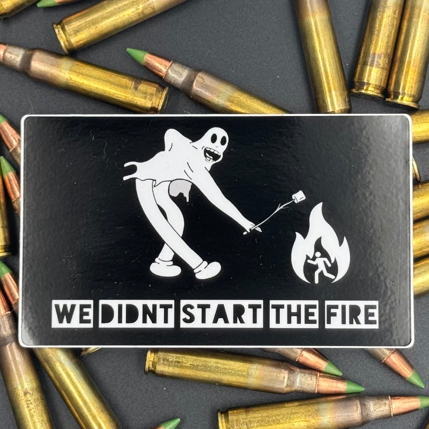 Sticker of a cartoon character in a ghost suit roasting a marshmallow over a fire on a bed of ammo
