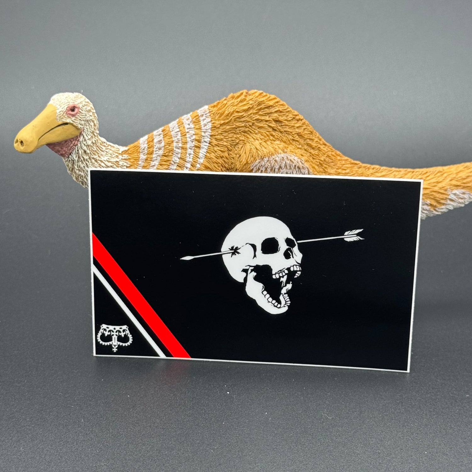 Sticker of a modern pirate flag with a skull with open mouth and arrow through the head and an upside down crown posing with a dinosaur