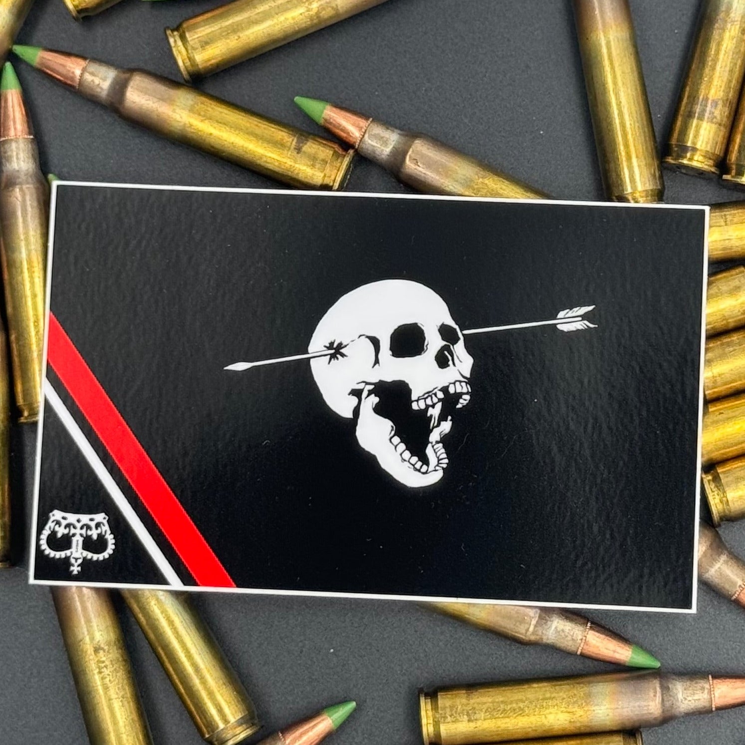 Sticker of a modern pirate flag with a skull with open mouth and arrow through the head and an upside down crown on a bed of ammo