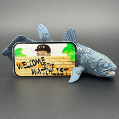 Sticker of an ATF agent peeking over a wall with the text 'Welcome to the Watchlist' posing with a Coelecanth