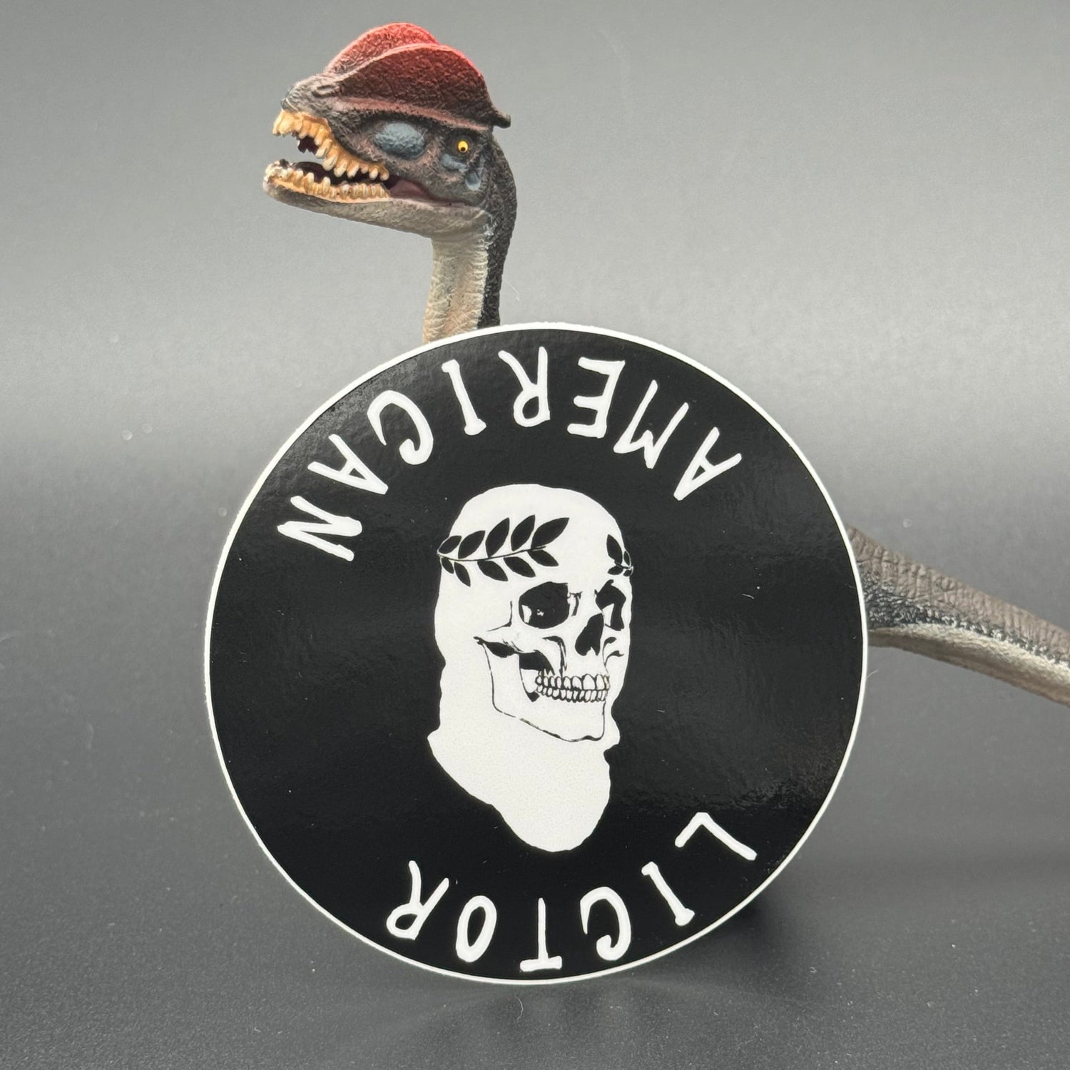 Sticker of the American Lictor Skull Logo in black posing with a dinosaur
