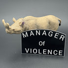 Black sticker with the text 'Manager of Violence' posing with a prehistoric mammal