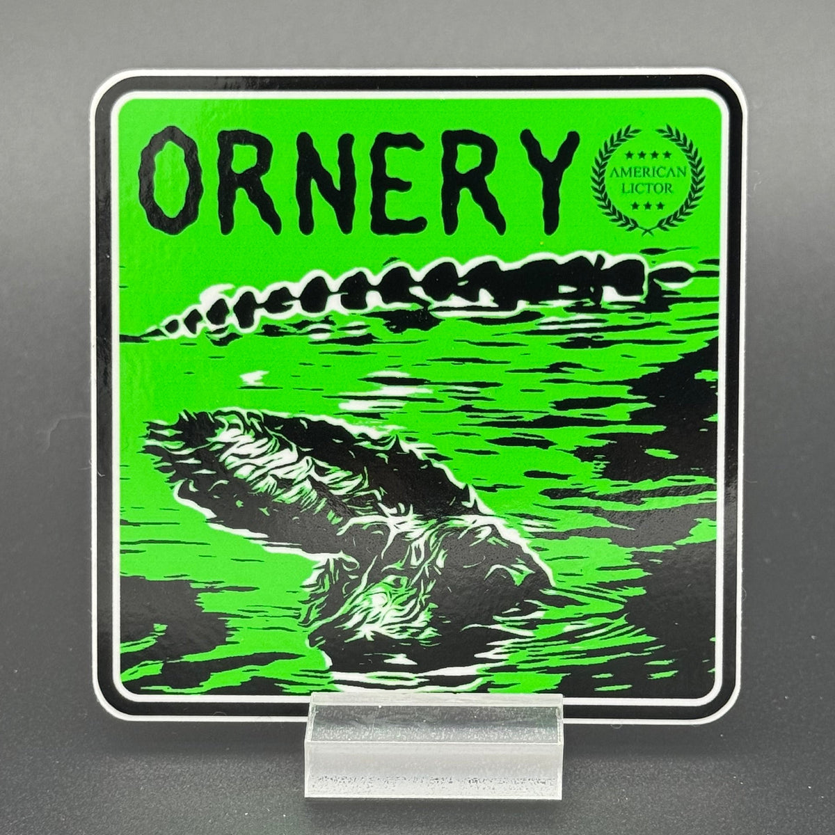 Black and green sticker of an alligator with the text 'Ornery'