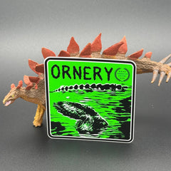 Black and green sticker of an alligator with the text 'Ornery' posed with a dinosaur
