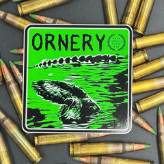 Black and green sticker of an alligator with the text 'Ornery' on a bed of ammo