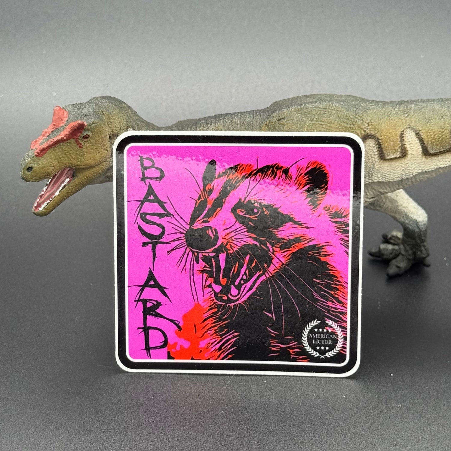 Black and Purple sticker of a badger with the text 'Bastard' posed with a dinosaur
