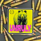 Yellow and pink Sticker of a grizzly bear with the text 'Unruly' on a bed of ammo