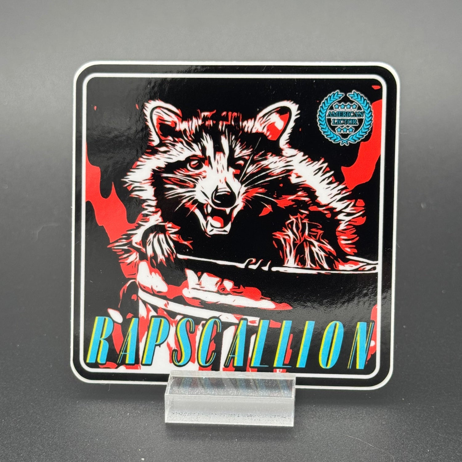 Black, red and teal Sticker of a Raccoon with the text 'Rapscallion'