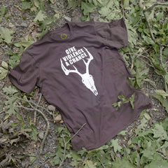 Brown t-shirt with white graphic and text on a ground with green leaves
